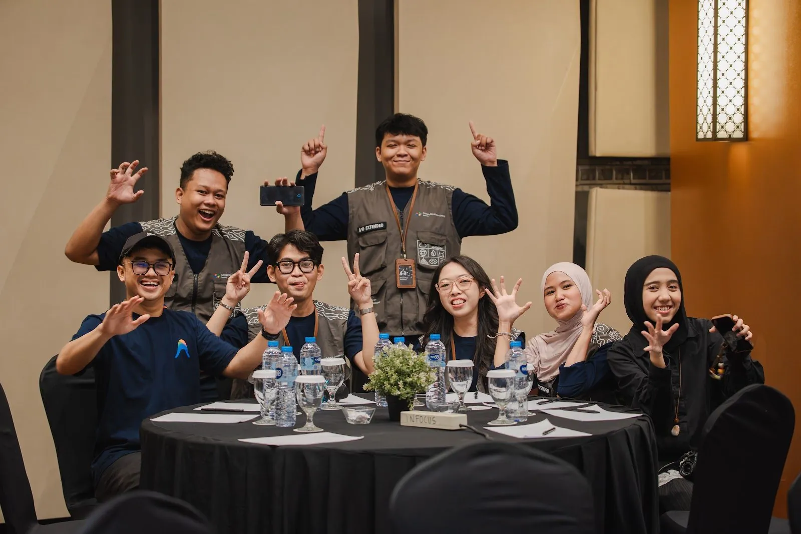 A group of attendees smiling and waving together around a table